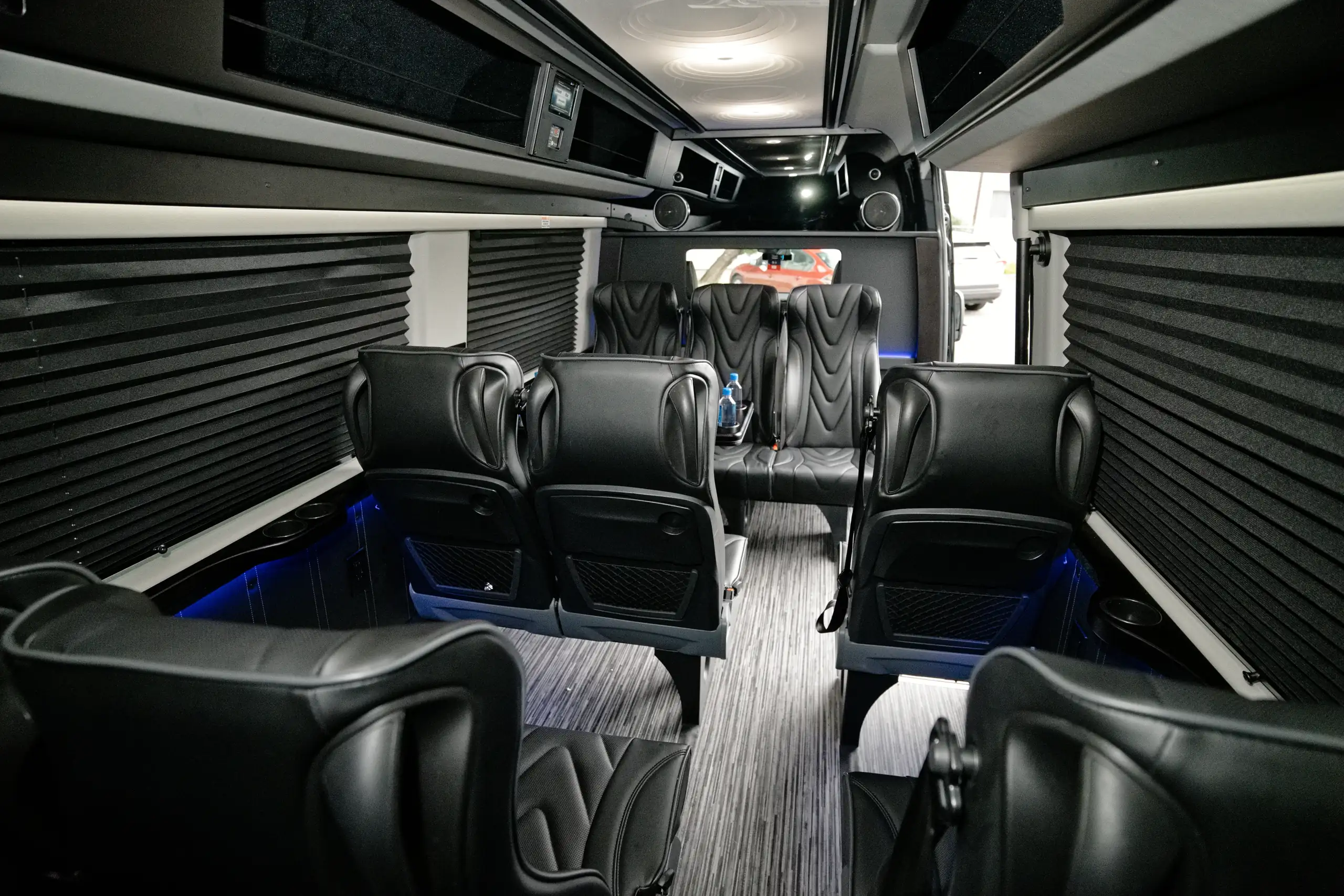 Aisle between black leather seats inside the Mercedes-Benz Executive Sprinter van, with blue floor lighting