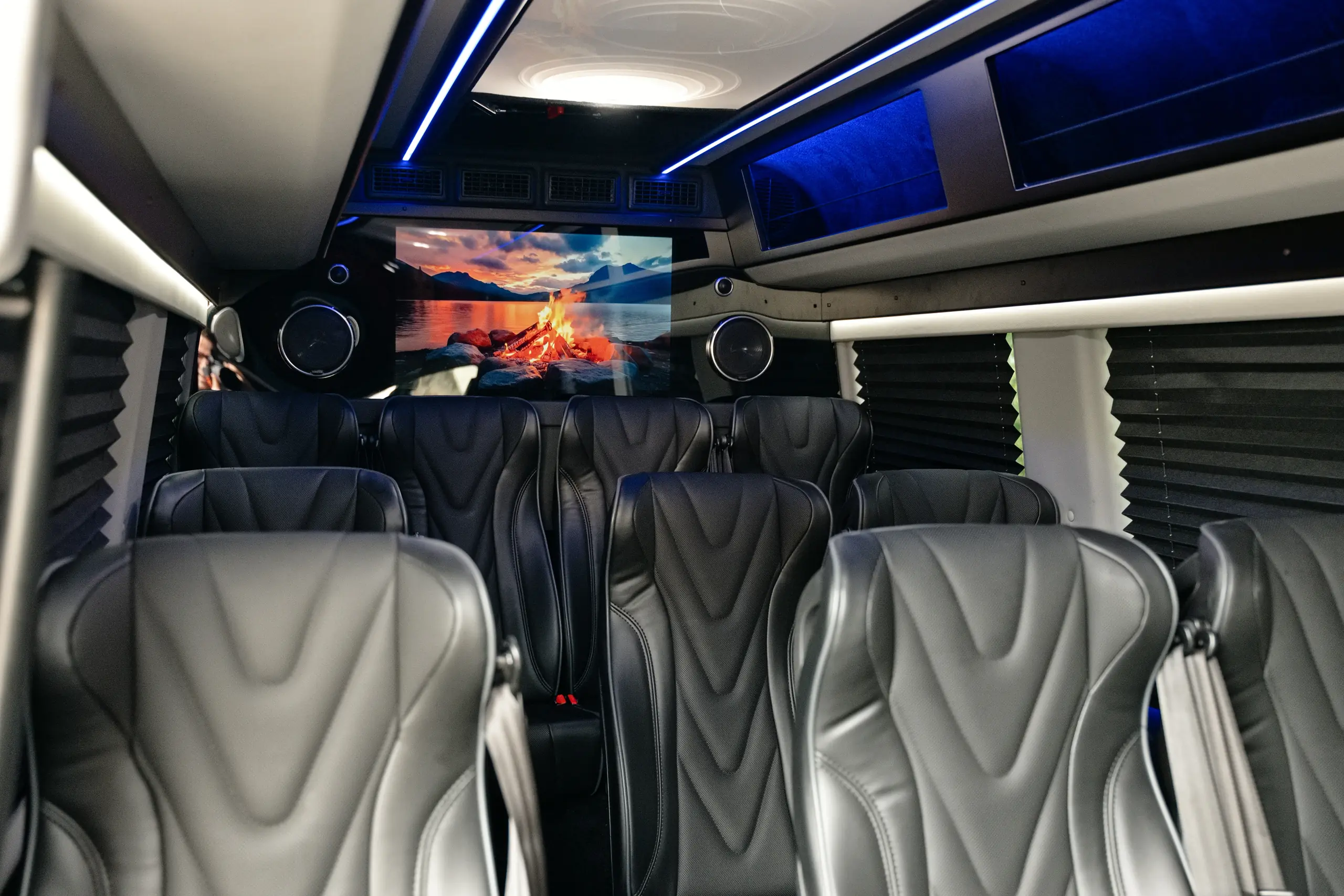 Interior of the Mercedes-Benz Executive Sprinter van with black leather seats, blue ambient lighting and a rear screen