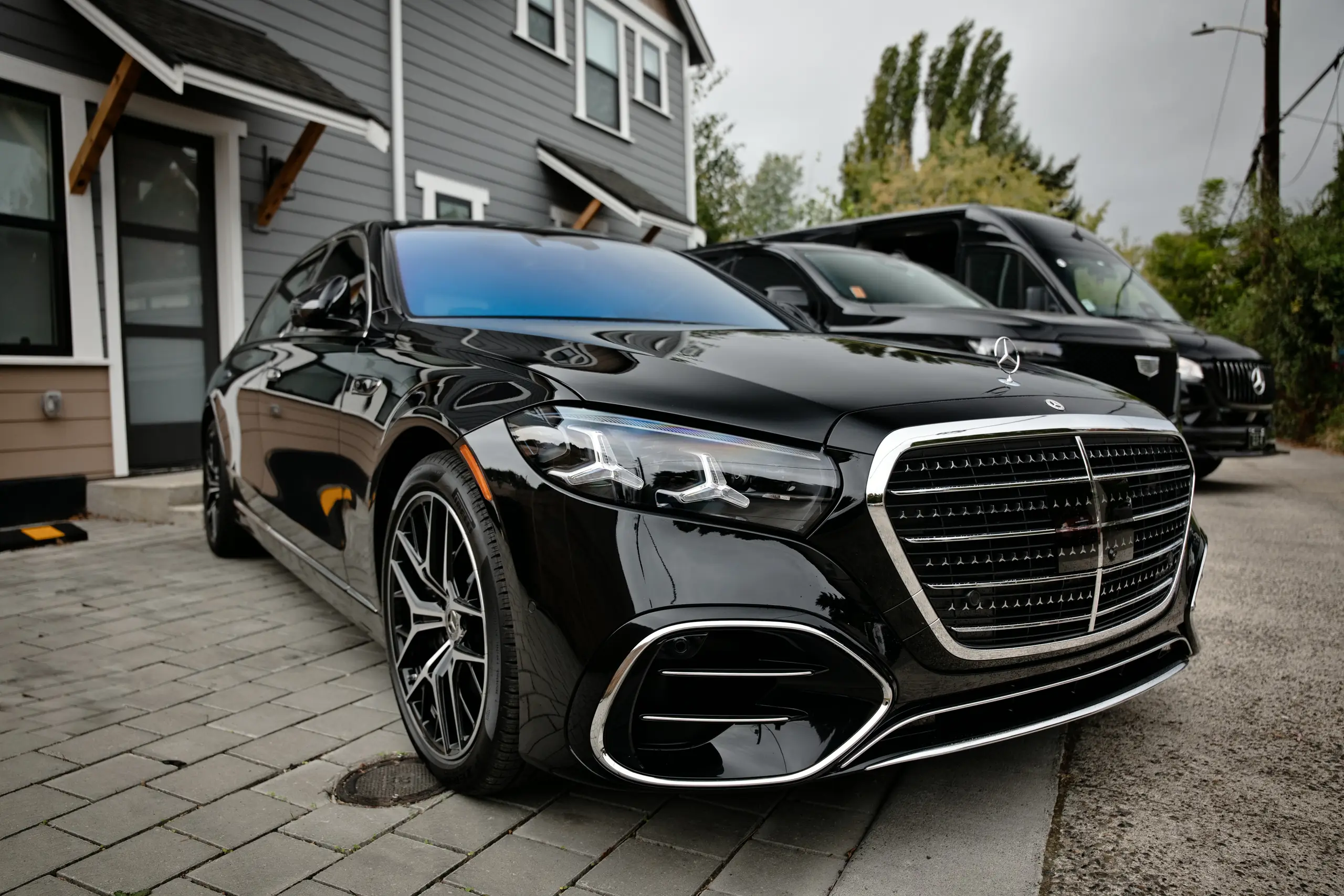 Black Mercedes-Benz S-Class first-class sedan in front three-quarter view with black vans parked behind it